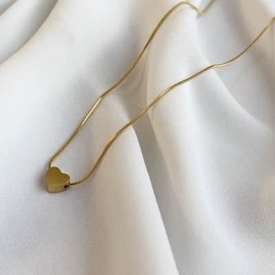 Colar dourado com pendente em forma de coração sobre tecido branco