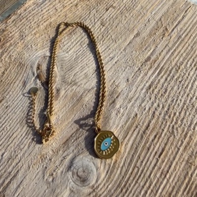 Colar dourado com pendente de olho azul sobre madeira clara