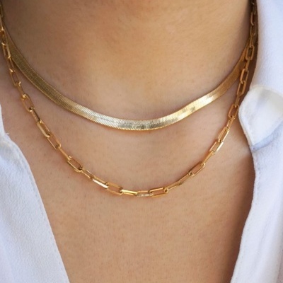 Duas correntes douradas de metal no pescoço de uma pessoa com camisa branca