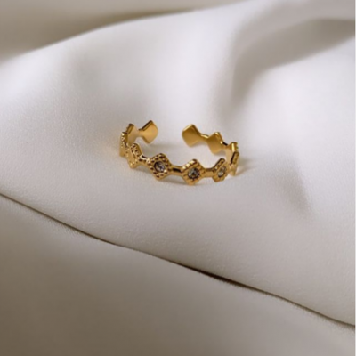 Anel dourado com padrão hexagonal sobre tecido branco