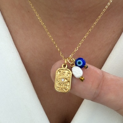 Colar dourado com pendente de olho, conta azul e duas pequenas contas, usado sobre roupa branca