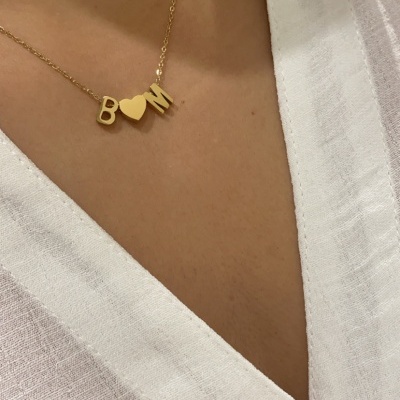 Colar dourado com letras B e M e coração entre elas, usado com camisa branca