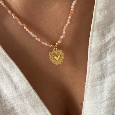 Colar de contas rosa com pendente dourado de coração em pessoa com blusa branca