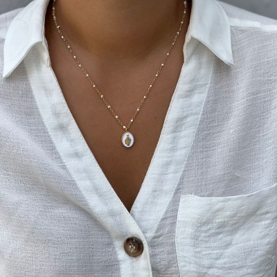 Colar dourado com pendente branco sobre camisa branca