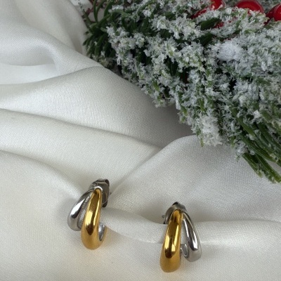 Brincos dourados e prateados sobre tecido branco com decoração de Natal ao fundo