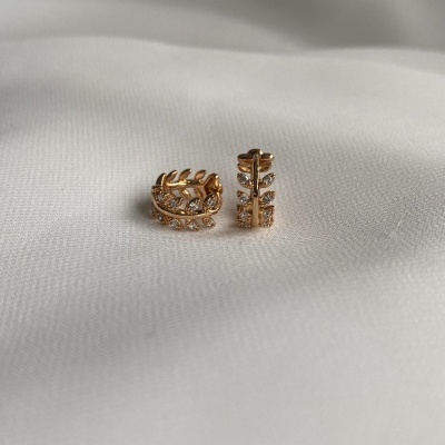 Par de brincos dourados em formato de folhas sobre tecido branco