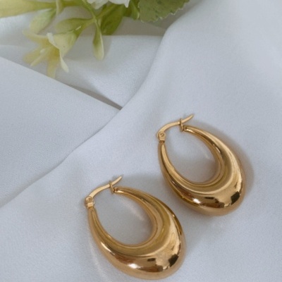 Brincos dourados em forma de gota com flores brancas ao fundo