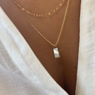 Duas correntes douradas com pendente retangular em madrepérola sobre pele e camisa branca