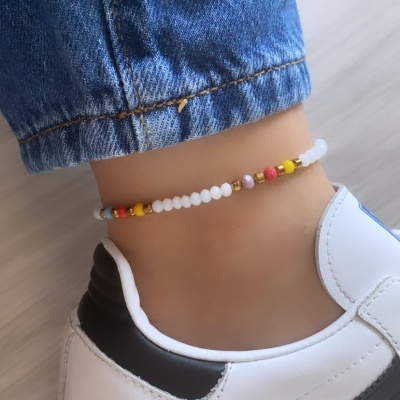 tornozeleira de contas coloridas em tornozelo com ténis branco e calça de ganga azul
