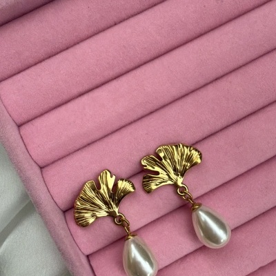 Brincos dourados com folha e pérola sobre estojo rosa