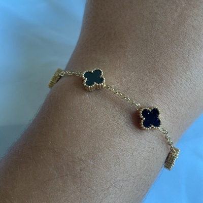 Pulseira dourada com trevos pretos no pulso