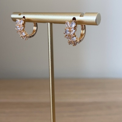 Brincos de argola dourados com pedras transparentes num suporte metálico dourado