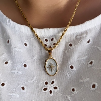 Colar dourado com pendente oval branco com estrela usado sobre blusa branca bordada