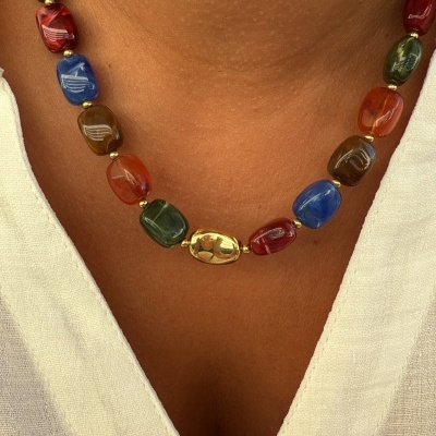 Colar colorido com conta dourada central sobre camisa branca