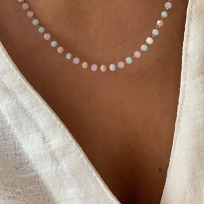 Colar com contas coloridas pastel e esferas douradas na pele, com camisa branca de tecido leve