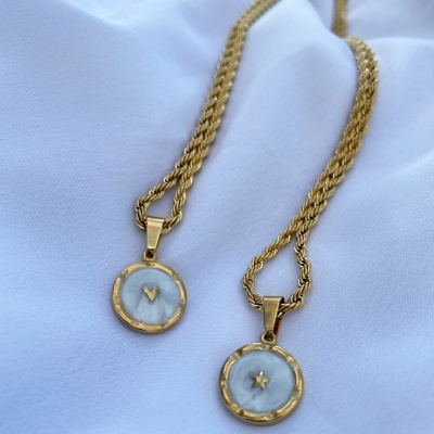 Dois colares dourados com pendentes redondos em madre-pérola com coração e estrela, sobre tecido branco