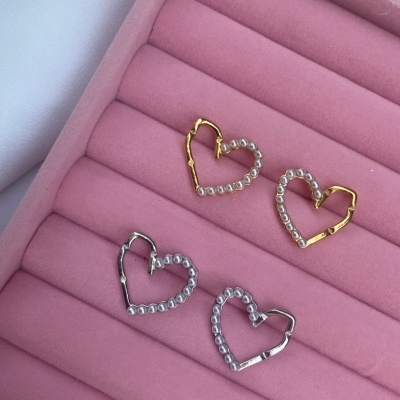 Brincos em forma de coração dourados e prateados com pérolas numa caixa rosa.