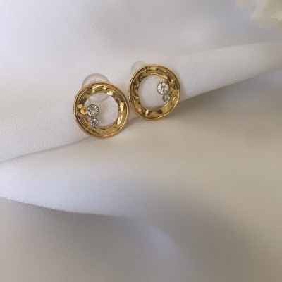 Brincos redondos dourados com pedras brilhantes sobre tecido branco