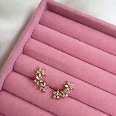 Brincos florais dourados com pedras em bandeja rosa.