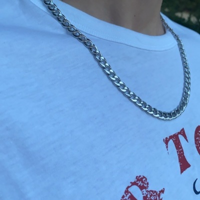 Corrente prateada de metal numa pessoa com t-shirt branca com texto vermelho e azul.