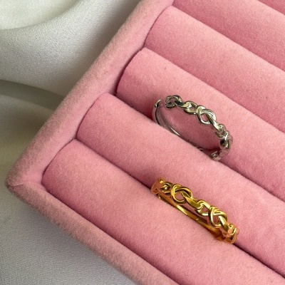 Duas alianças entrelaçadas, prateada e dourada, numa caixa rosa acolchoada.