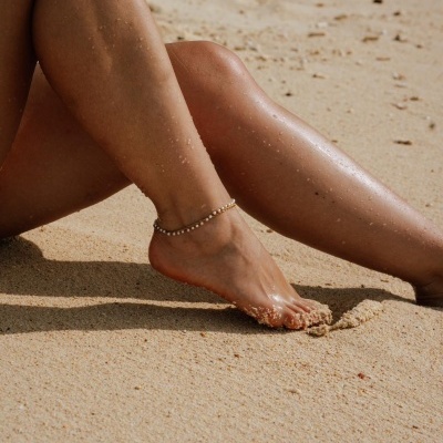 Pernas femininas bronzeadas na areia da praia com bracelete prateado no pé