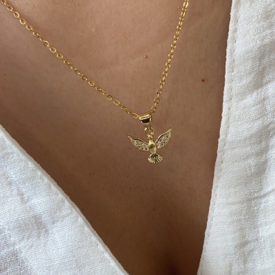 Colar dourado com pendente de pássaro usado sobre camisa branca