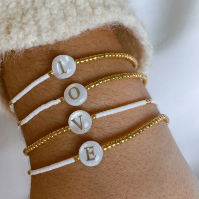Pulseiras com letras brancas formando LOVE num pulso, com camisola creme felpuda ao fundo