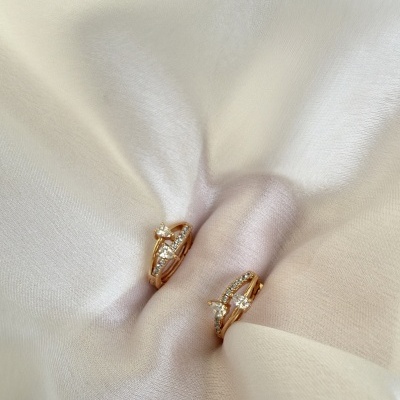 Brincos dourados com pedras brilhantes sobre tecido branco sedoso