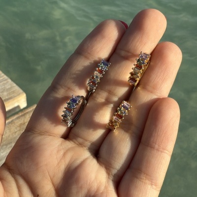 Brincos com pedras coloridas na mão junto a água e um deck de madeira