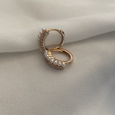 Par de argolas douradas com pérolas e cristais sobre tecido bege