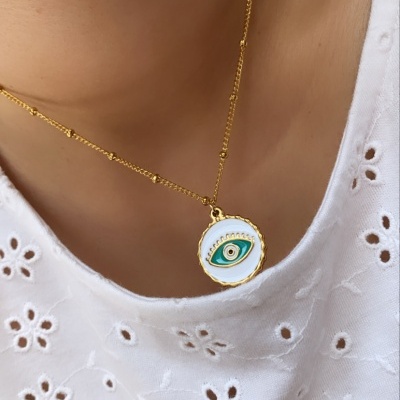 Colar dourado com pendente redondo de olho estilizado em blusa branca bordada