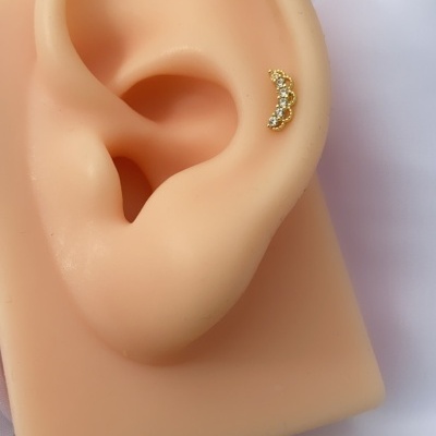 Brinco dourado com pedras em orelha de silicone sobre tecido branco