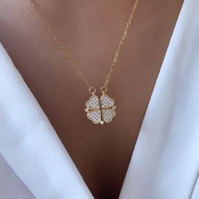 Colar dourado com pendente de trevo com brilhantes num pescoço com blusa branca