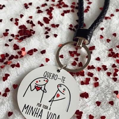 Porta-chaves redondo branco com desenho e texto em português e pega preta sobre superfície com confetes em forma de coração