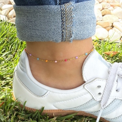 Tornozelo com pulseira colorida, calça de ganga azul e sapatilha branca em relvado