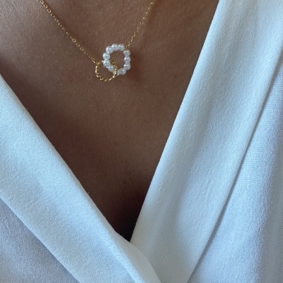 Colar dourado com pendentes de pérolas e metal, usado com camisa branca.