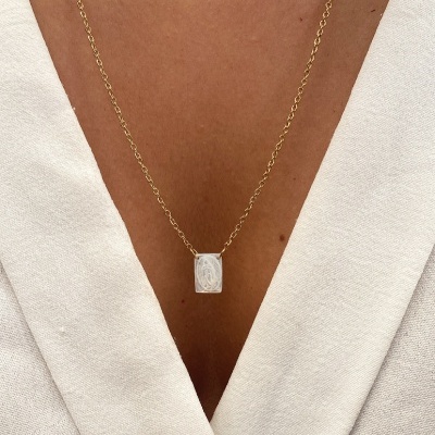 Colar em corrente dourada com pendente retangular prateado no pescoço de pessoa com camisa branca