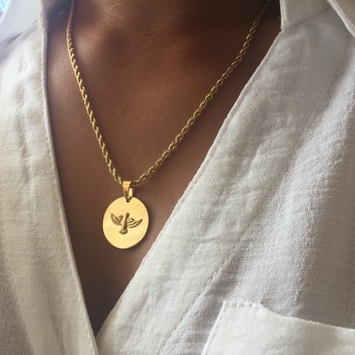 Colar dourado com pendente redondo com símbolo de inseto numa camisa branca de linho.