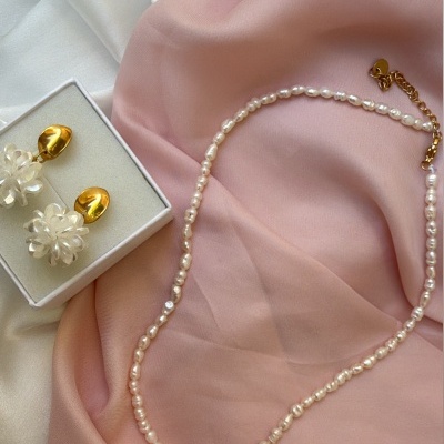 Colar de pérolas e brincos dourados com flores transparentes sobre tecidos branco e rosa
