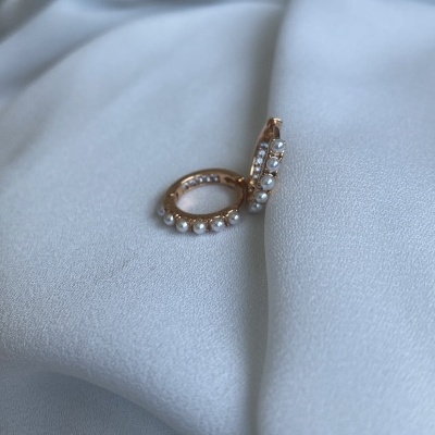 Brincos de argola dourados com pérolas sobre tecido branco