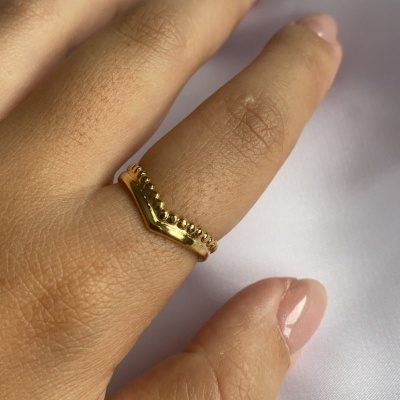 Anel dourado em V com bolinhas, mão feminina em tecido branco