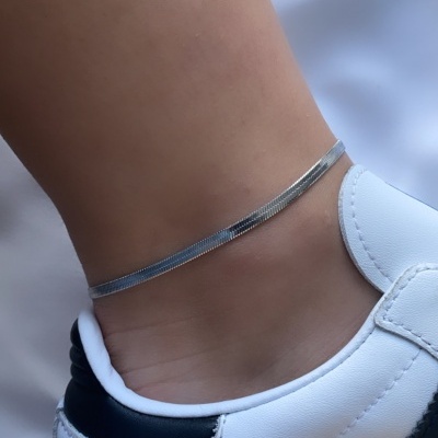 Pulseira fina no tornozelo e parte de ténis branco com detalhes a preto