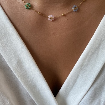 Colar dourado com flores coloridas num pescoço vestindo camisola branca