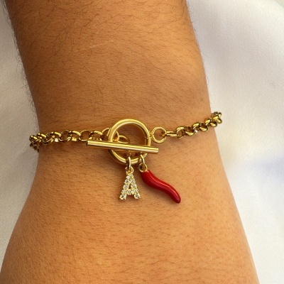 Pulseira dourada com pendentes vermelho e letra A num pulso