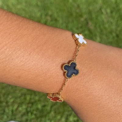 Pulseira dourada com pingentes em forma de trevo em branco, preto e castanho ao pulso