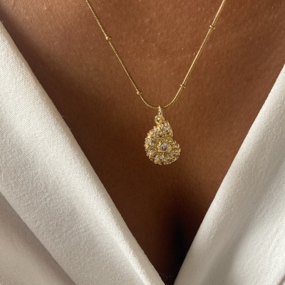 Colar dourado com pendente espiral e cristais sobre pele e roupa branca