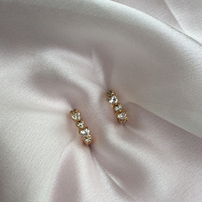 Brincos dourados com pedras transparentes sobre tecido branco acetinado