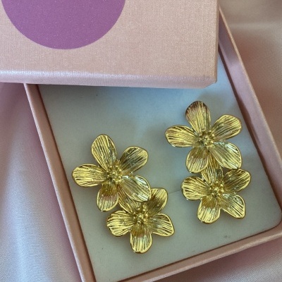 Brincos dourados em forma de flores em caixa de joias rosa.