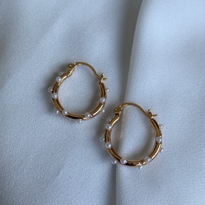 Brincos argola dourados com pérolas sobre tecido branco